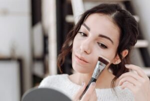 woman putting on a make up while looking in the mirror
